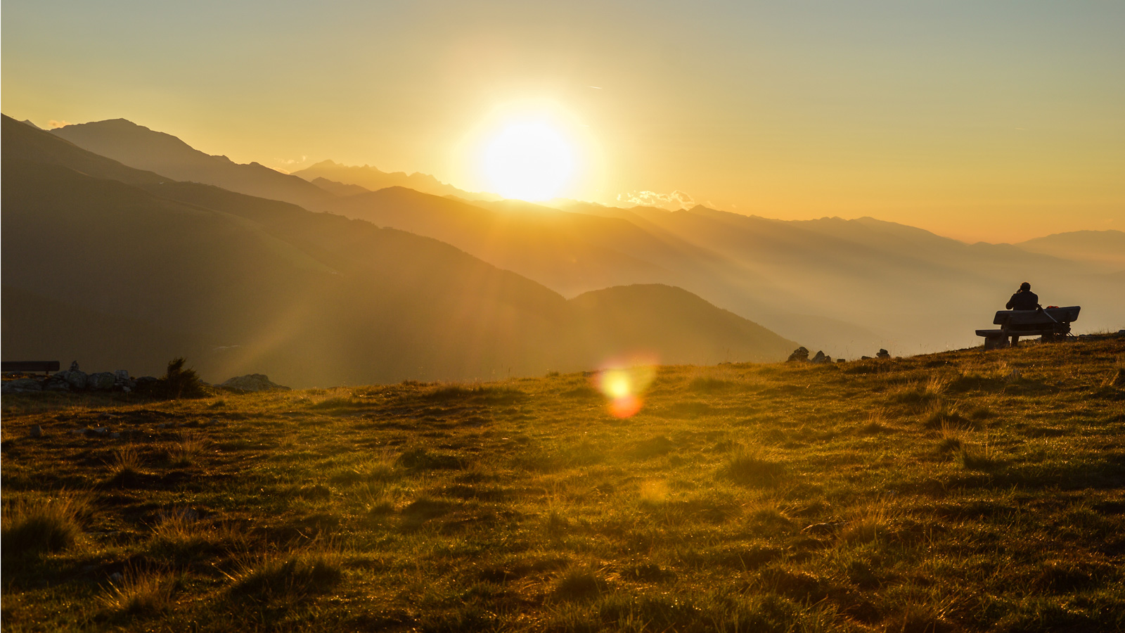 Un uomo siede su una panchina e si gode il tramonto sulle Dolomiti presso Rio Pusteria